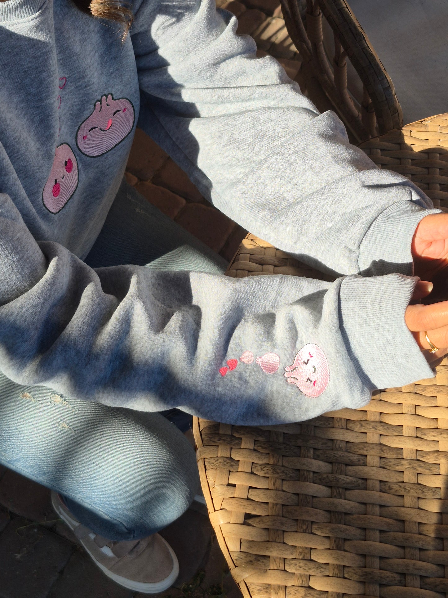 Outdoor shot of a person wearing the grey Kawaii Dumpling embroidered unisex sweatshirt, highlighting the sleeve embroidery with pink hearts and dumpling