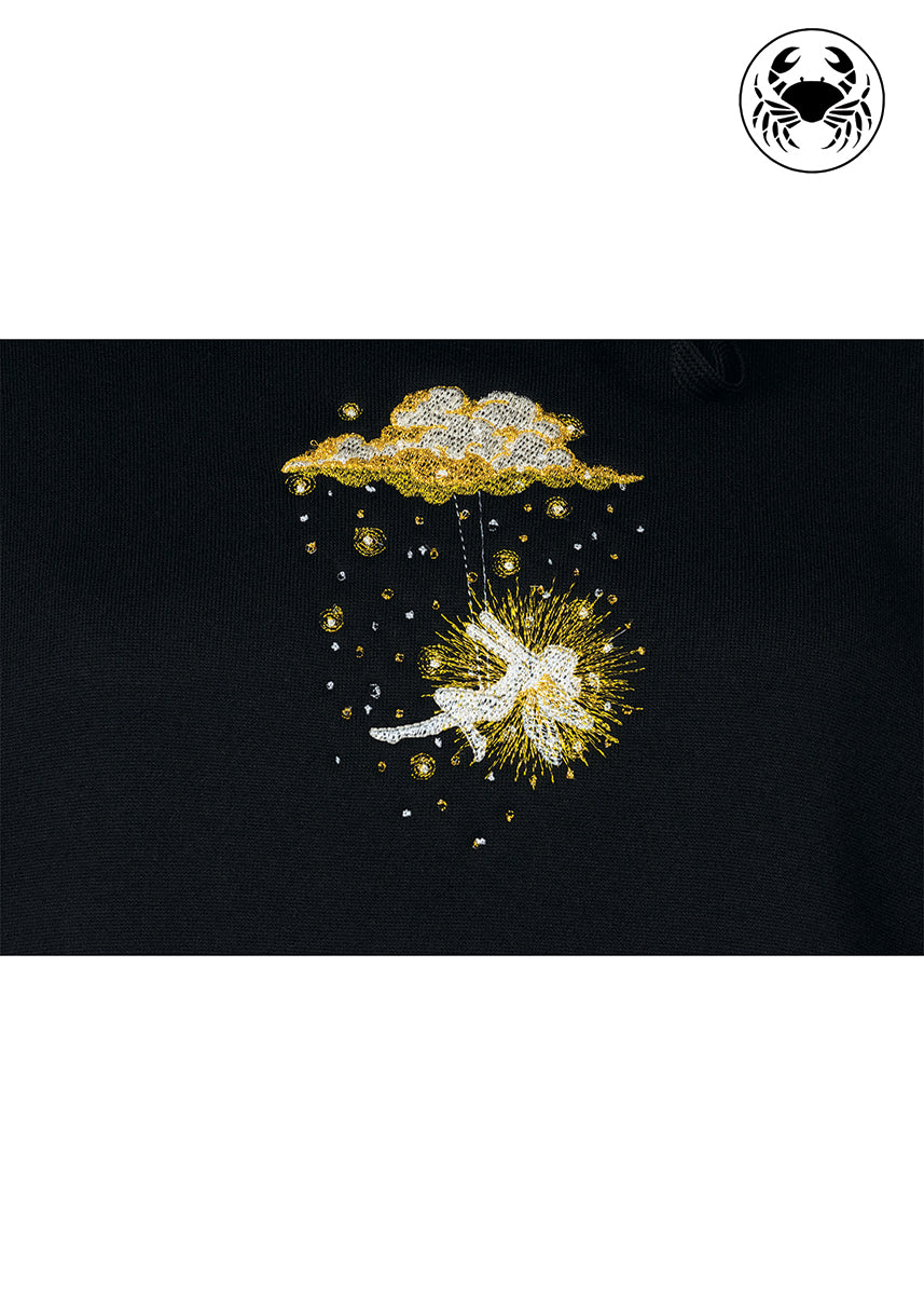 Close-up of golden embroidered fairy swinging beneath a glowing cloud on black hoodie, Canadian apparel