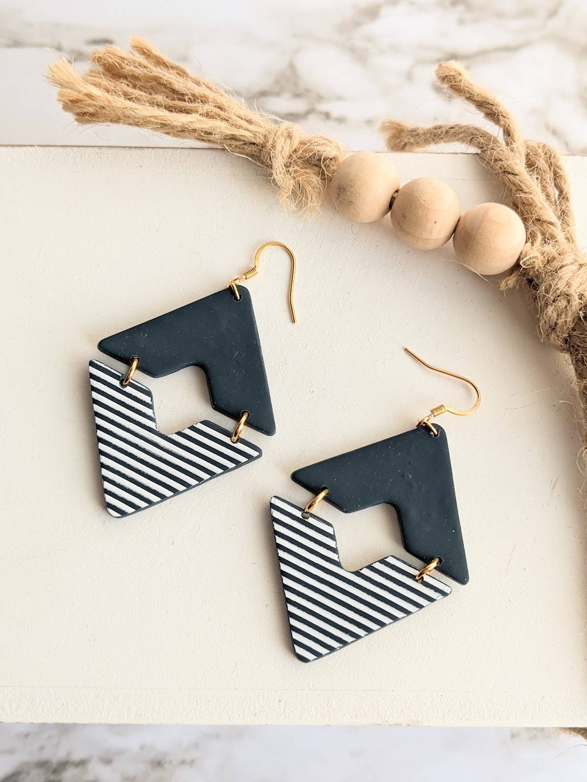 Pair of Elizabeth Clay Dangle Earrings, featuring handmade geometric polymer clay shapes in black and striped white patterns with gold hooks