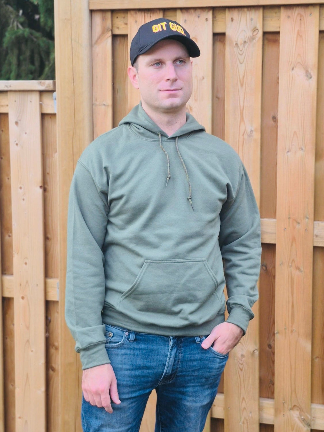Male model wearing unisex military green hoodie with drawstring hood and front pocket