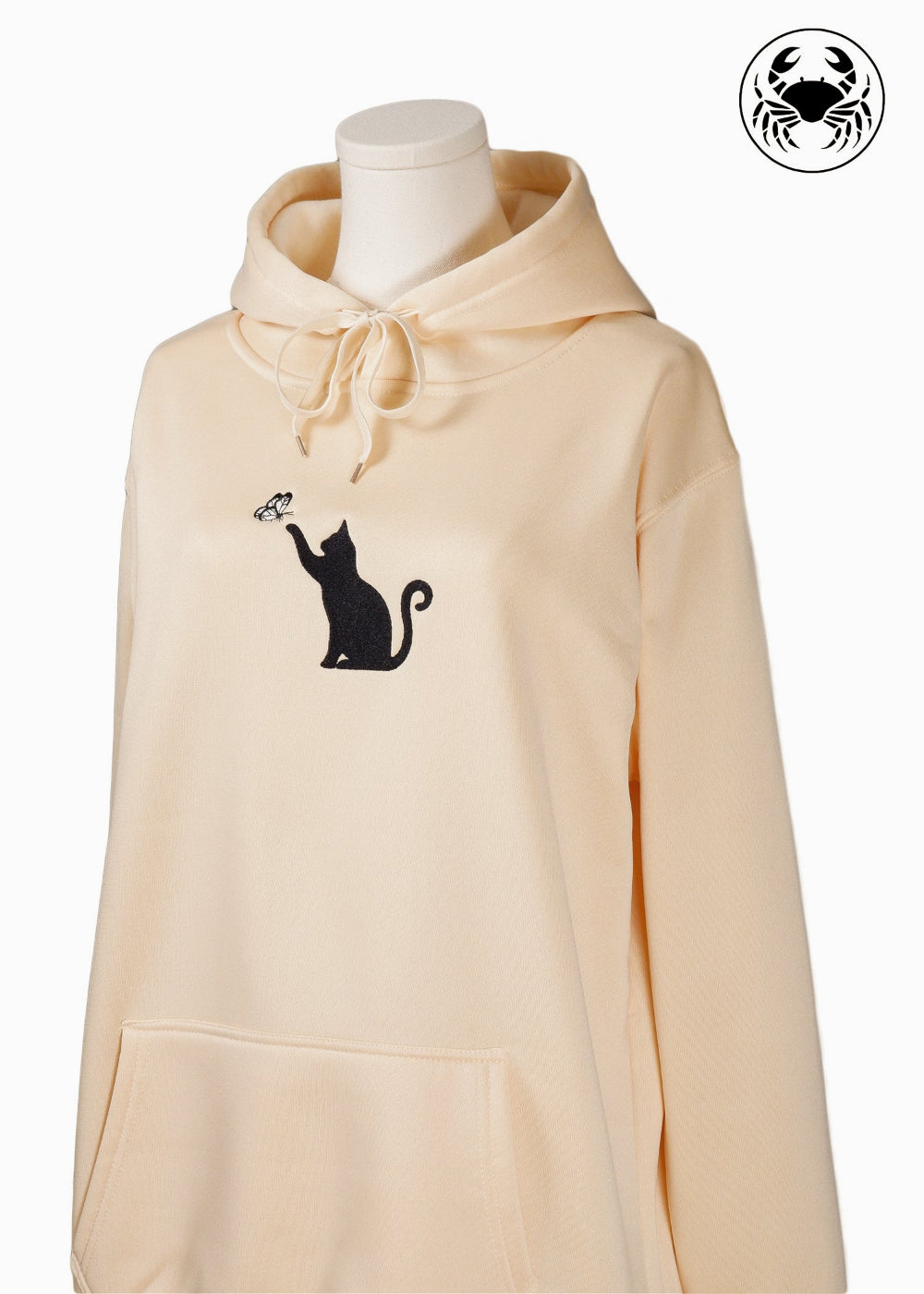 angled view of Unisex beige hoodie with a front kangaroo pocket, drawstring hood, and an embroidered chest design featuring a Cat Caught in a Moment with Butterfly