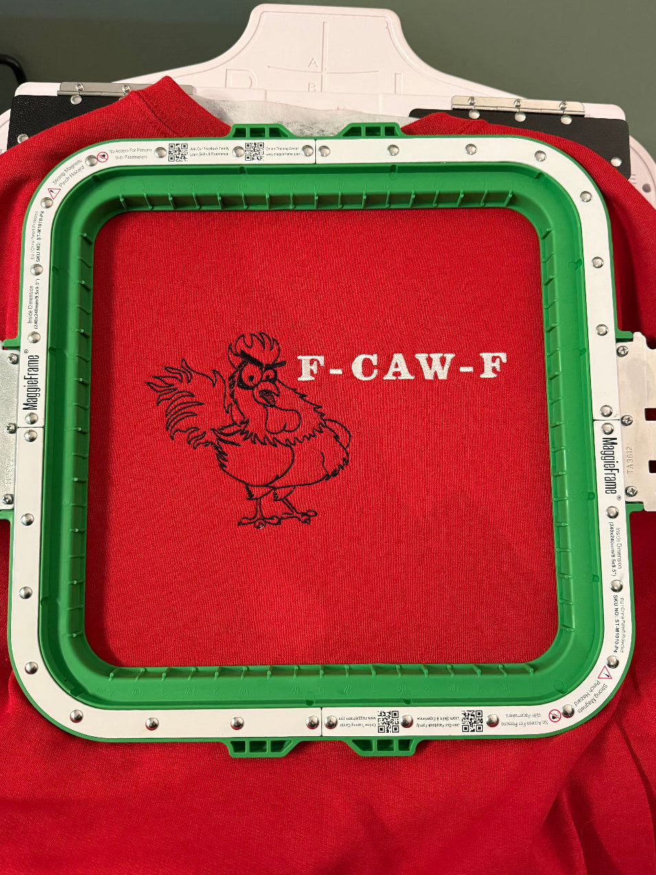 Embroidery machine hoop with red sweatshirt and 'F-CAW-F' design embroidery