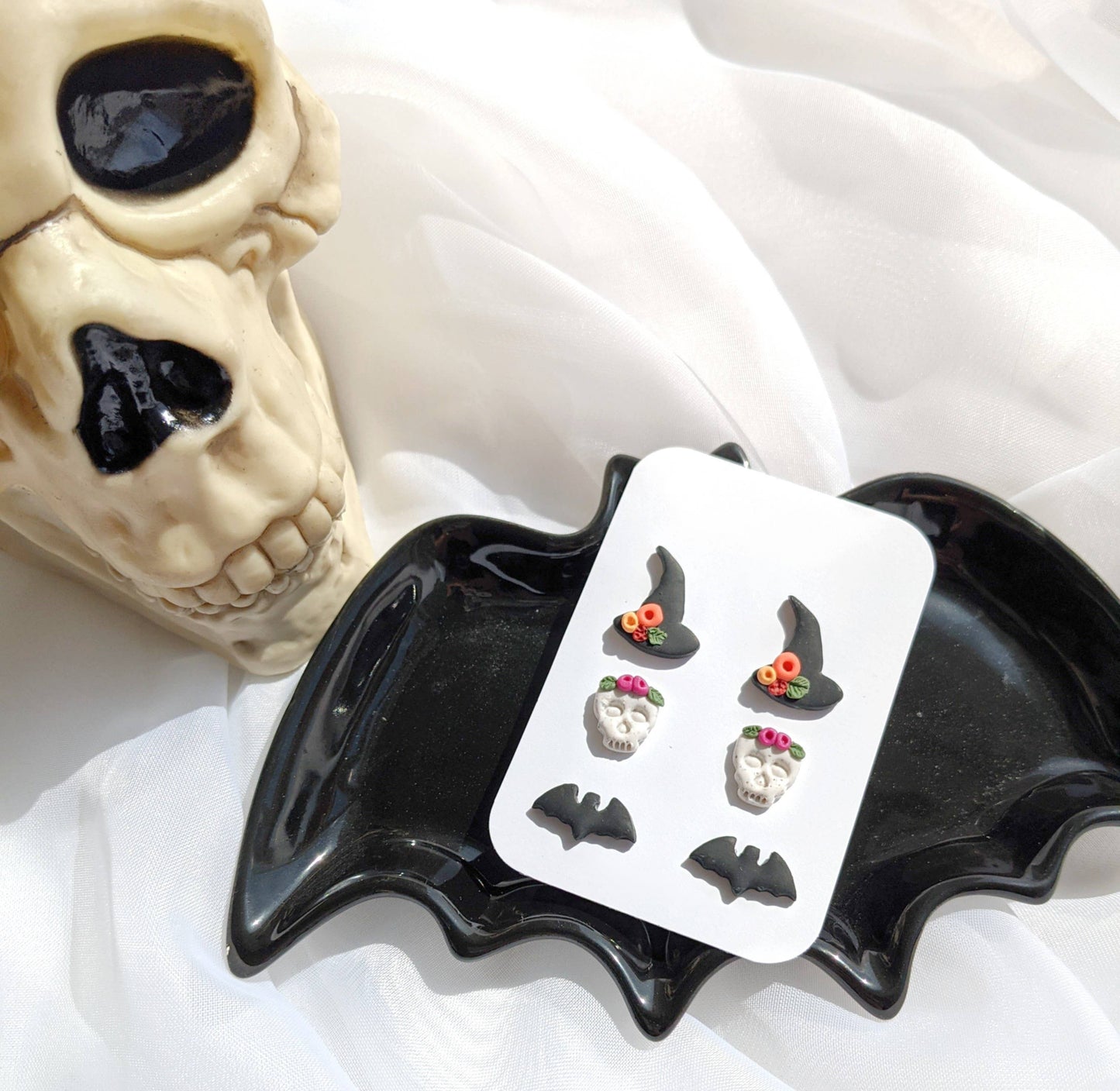 Halloween Theme Stud Pack 2, featuring three pairs of handmade polymer clay studs: black witch hats with flowers, white skulls with floral crowns, and matte black bats