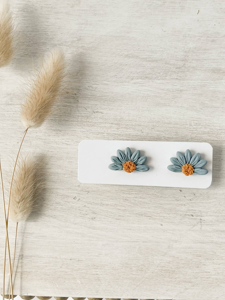 Pair of handmade polymer clay Aurora stud earrings featuring blue daisy design with textured yellow center