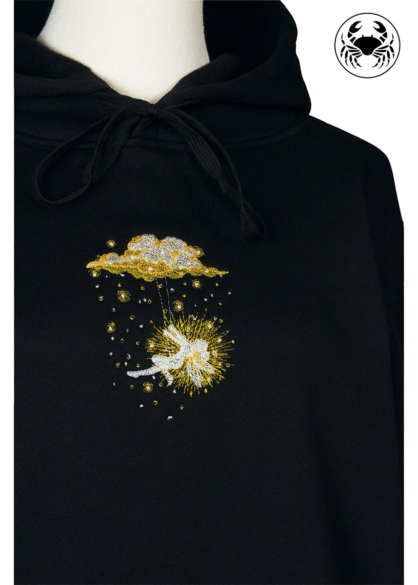 Close-up of golden embroidered fairy swinging beneath a glowing cloud on black hoodie, Canadian apparel
