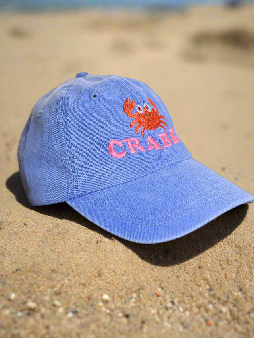 Blue baseball cap with an embroidered red cartoon crab and the word “CRABBY” in pink text