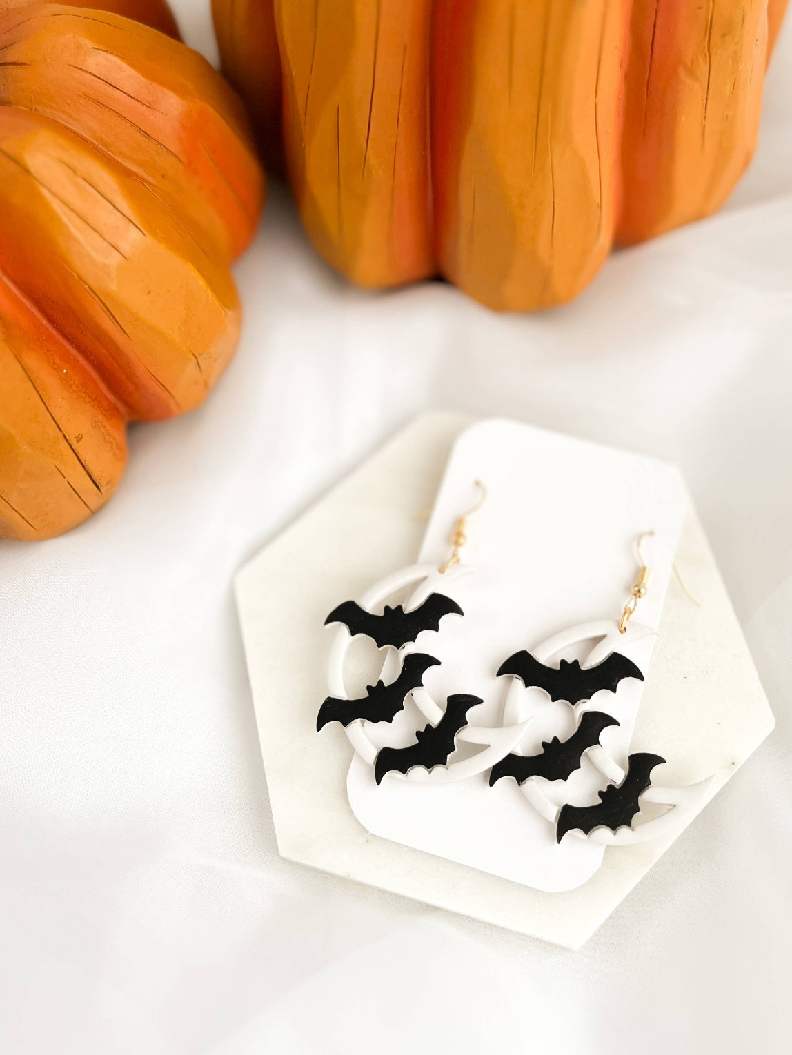 Pair of Halloween Dangle Earrings, featuring handmade black bats flying over white crescent moons, crafted from polymer clay and hanging from gold color hooks