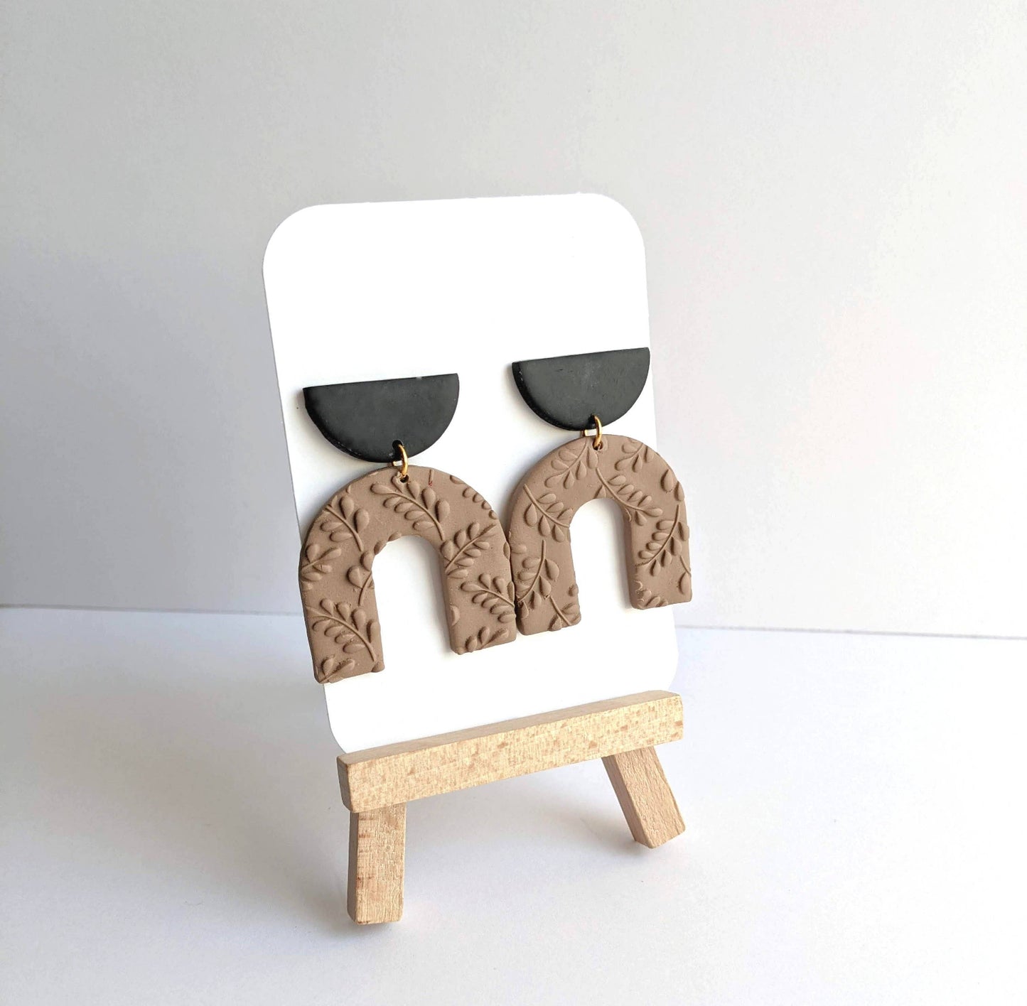 Pair of Harper Dangle Earrings, featuring handmade polymer clay arches with botanical impressions and matte black semicircle tops