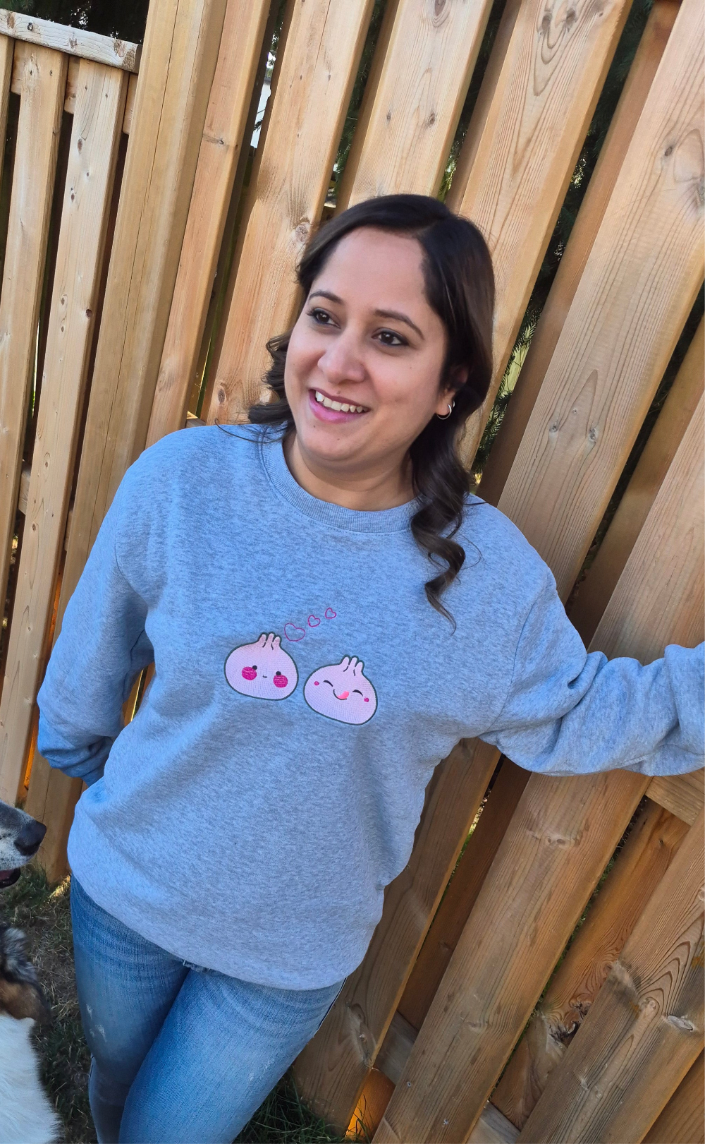 Person standing outdoors wearing a grey Kawaii Dumpling embroidered unisex sweatshirt with cute dumpling graphics on the chest.