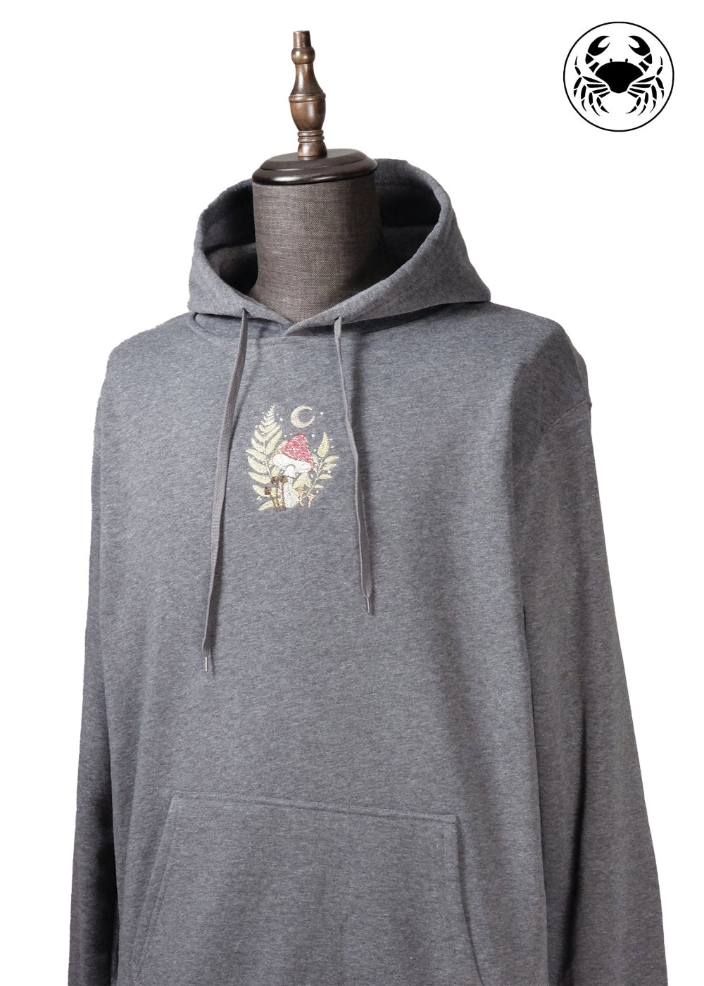 Angled view of Unisex charcoal gray fleece hoodie with a front kangaroo pocket, drawstring hood, and a chest graphic featuring a mushroom and botanical leaves