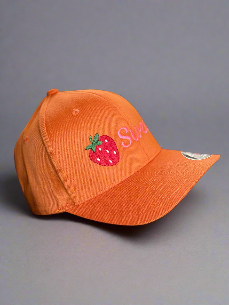 Side angle of the orange Sweet cap, showing red strawberry design and visor sticker