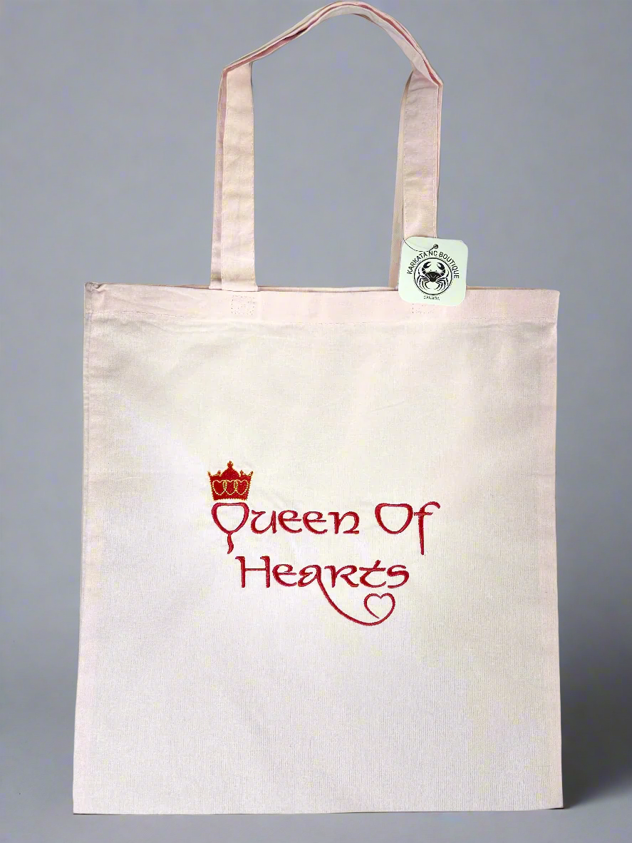 Light pink canvas tote bag with “Queen of Hearts” red embroidered text and a gold crown stitched above the design.