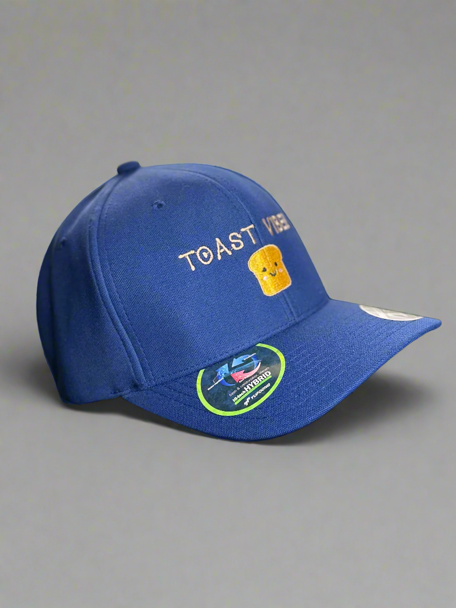  A royal blue baseball cap viewed from the side, showing the “TOAST VIBES” embroidery and toast design, with product stickers on the brim