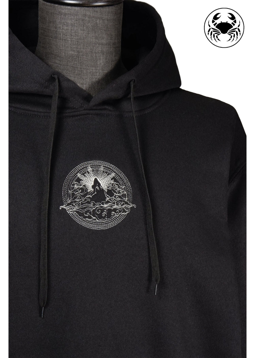 Closeup view of Unisex black fleece hoodie featuring a front kangaroo pocket, adjustable drawstring hood, and an embroidered  mountain and sun rising design 