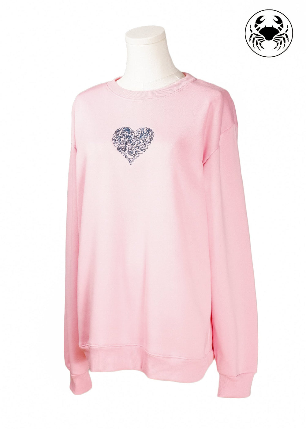 tilted view of Light pink unisex crewneck sweatshirt featuring a embroidered heart design on the chest, long sleeves, ribbed cuffs and hem