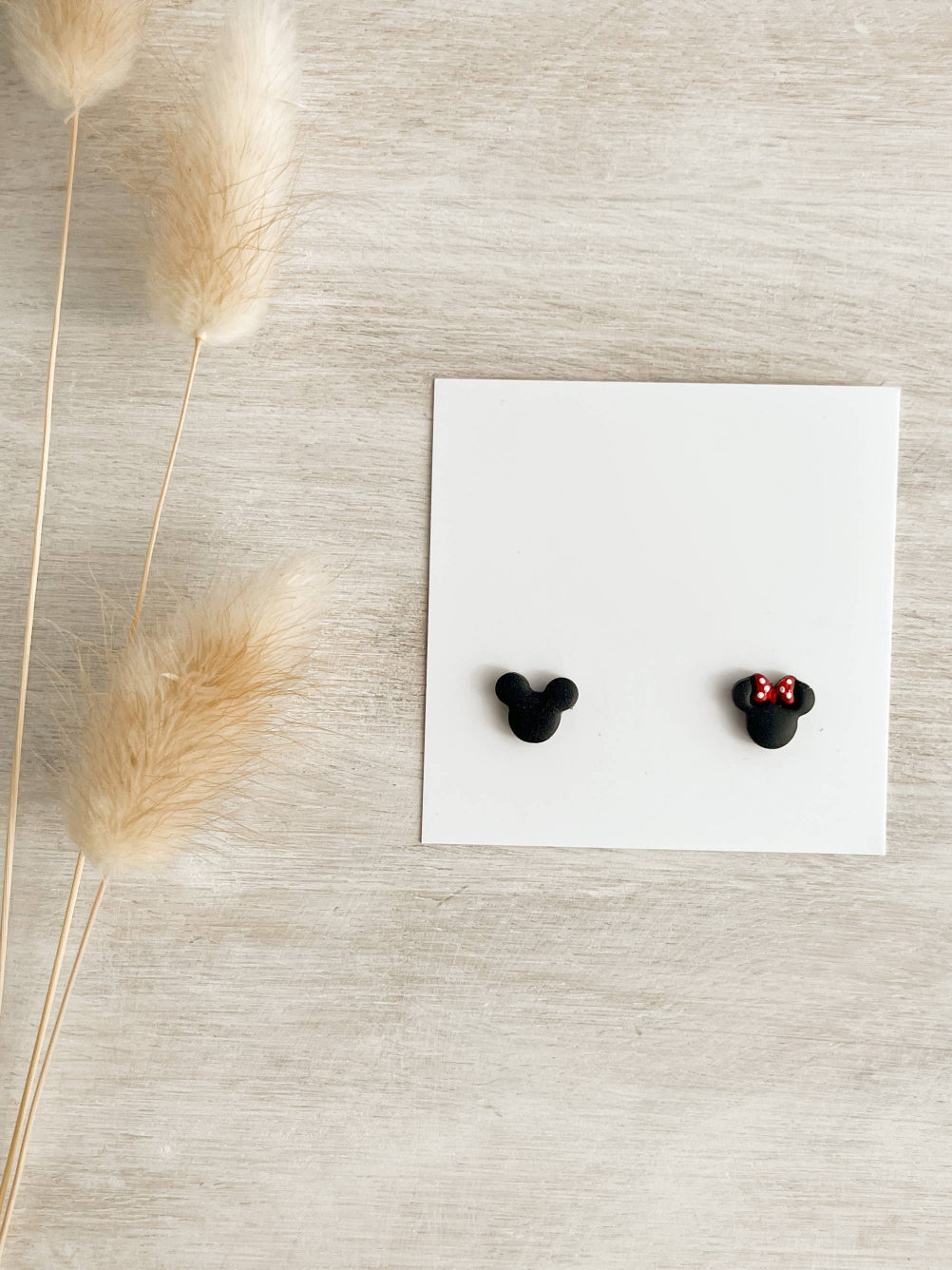 Pair of Magic Ears Micro Stud Earrings, featuring handmade polymer clay studs in black mouse head shapes, one adorned with a red polka dot bow