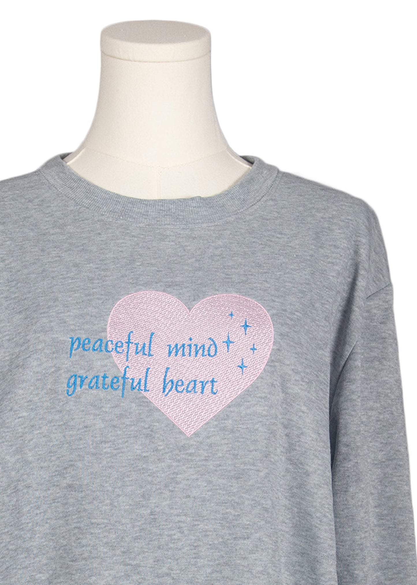 Close-up of light grey sweatshirt with “peaceful mind, grateful heart” embroidered text, Canadian apparel
