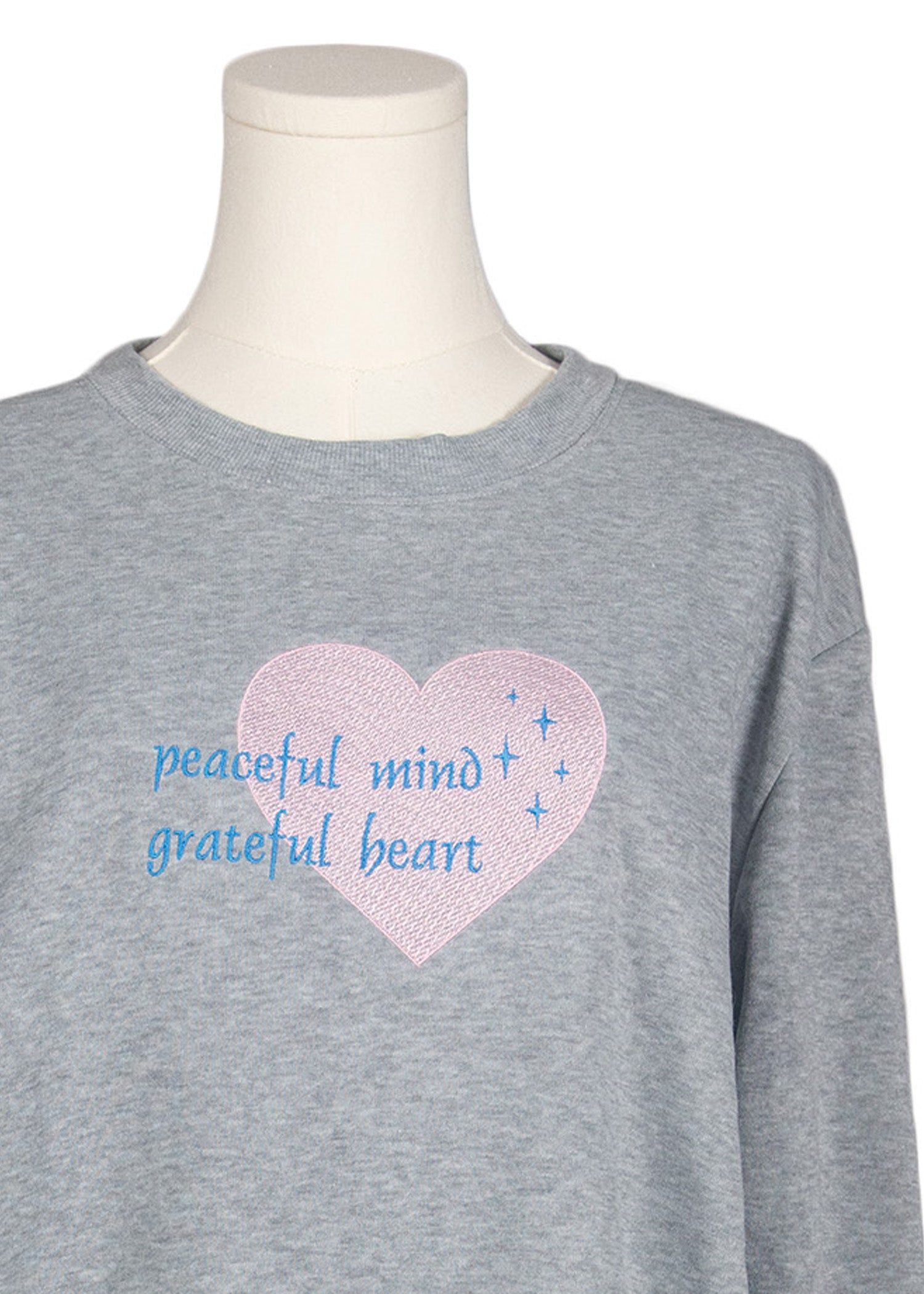 Close-up of light grey sweatshirt with “peaceful mind, grateful heart” embroidered text, Canadian apparel