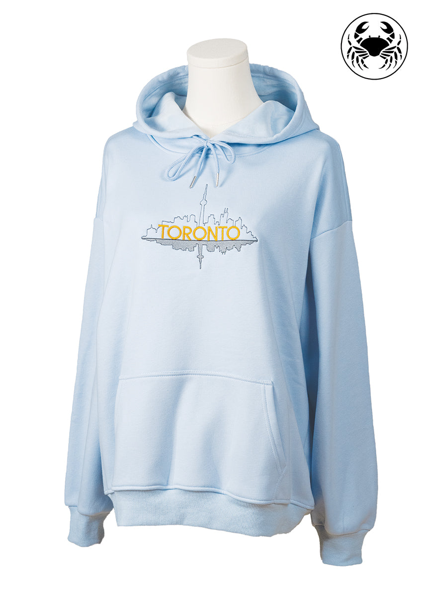 Front angled view of sky blue hoodie with embroidered Toronto skyline outline, Canadian apparel