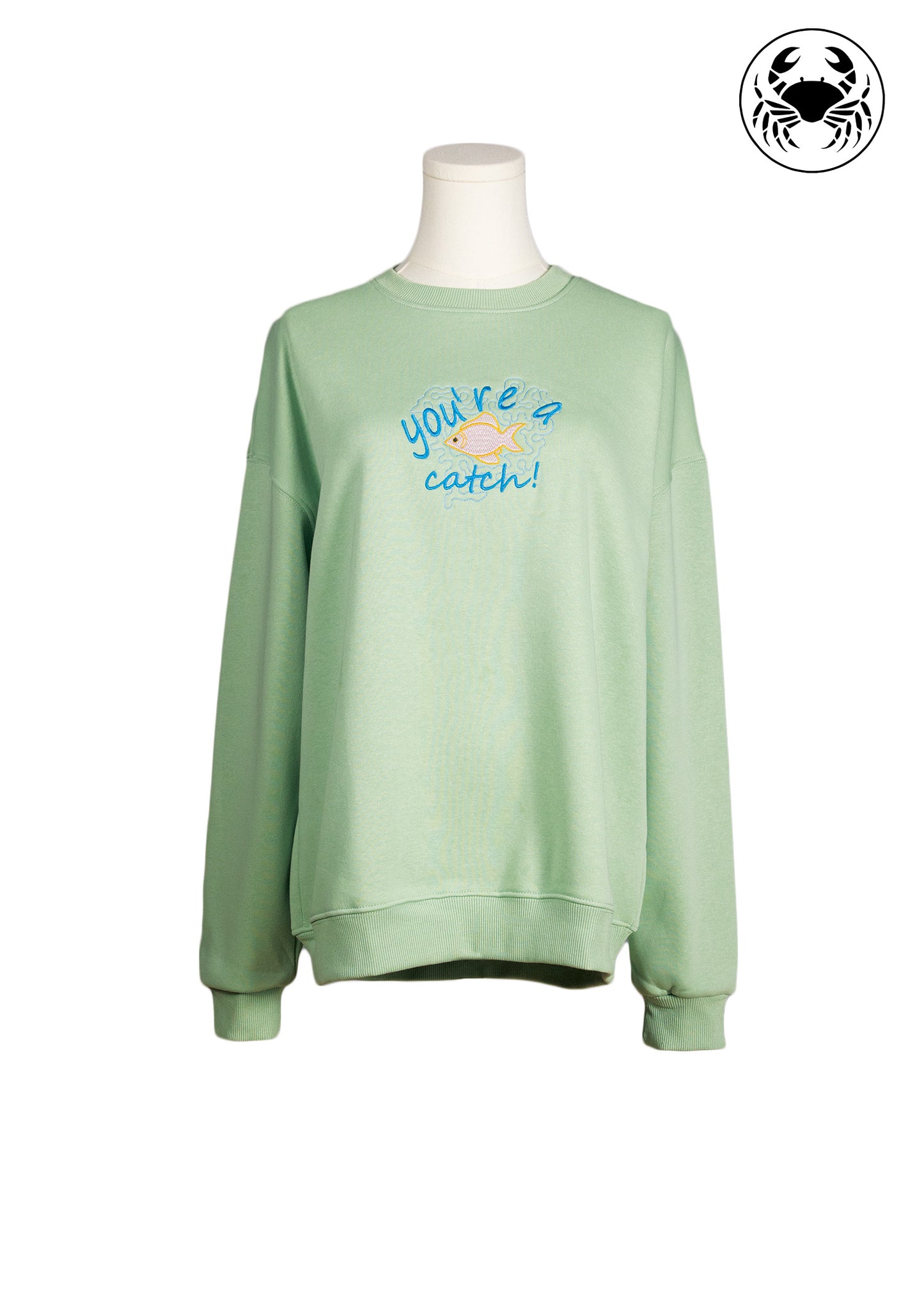 Front view of pastel green sweatshirt with “you’re a catch” fish embroidery, Canadian apparel